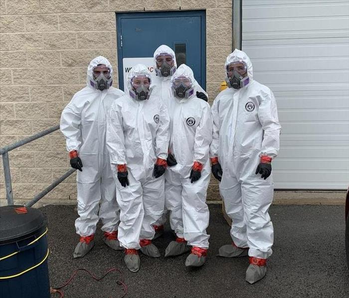 Five SERVPRO of Barrie employees dressed in white hazmat suits, standing in front of a Canadian warehouse building.