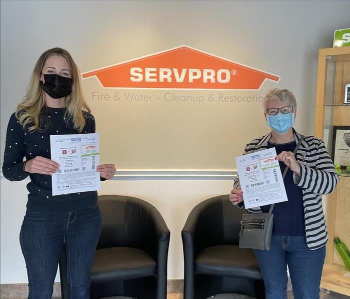 SERVPRO employee standing with contest winner holding paper tickets infront of company logo.
