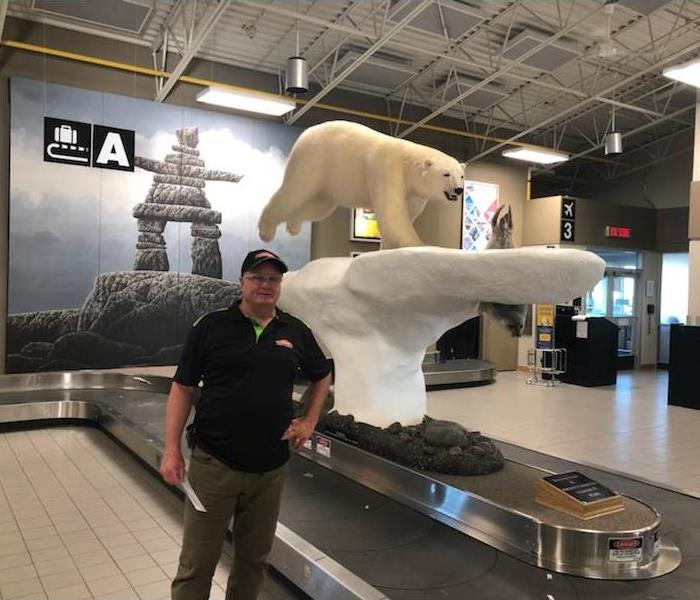 SERVPRO of Barrie technician standing by the Kugluktuk Airport Polar Bear statue in Nunavut, beside baggage claim belt
